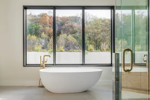Freestanding soaking tub beside floor-to-ceiling windows